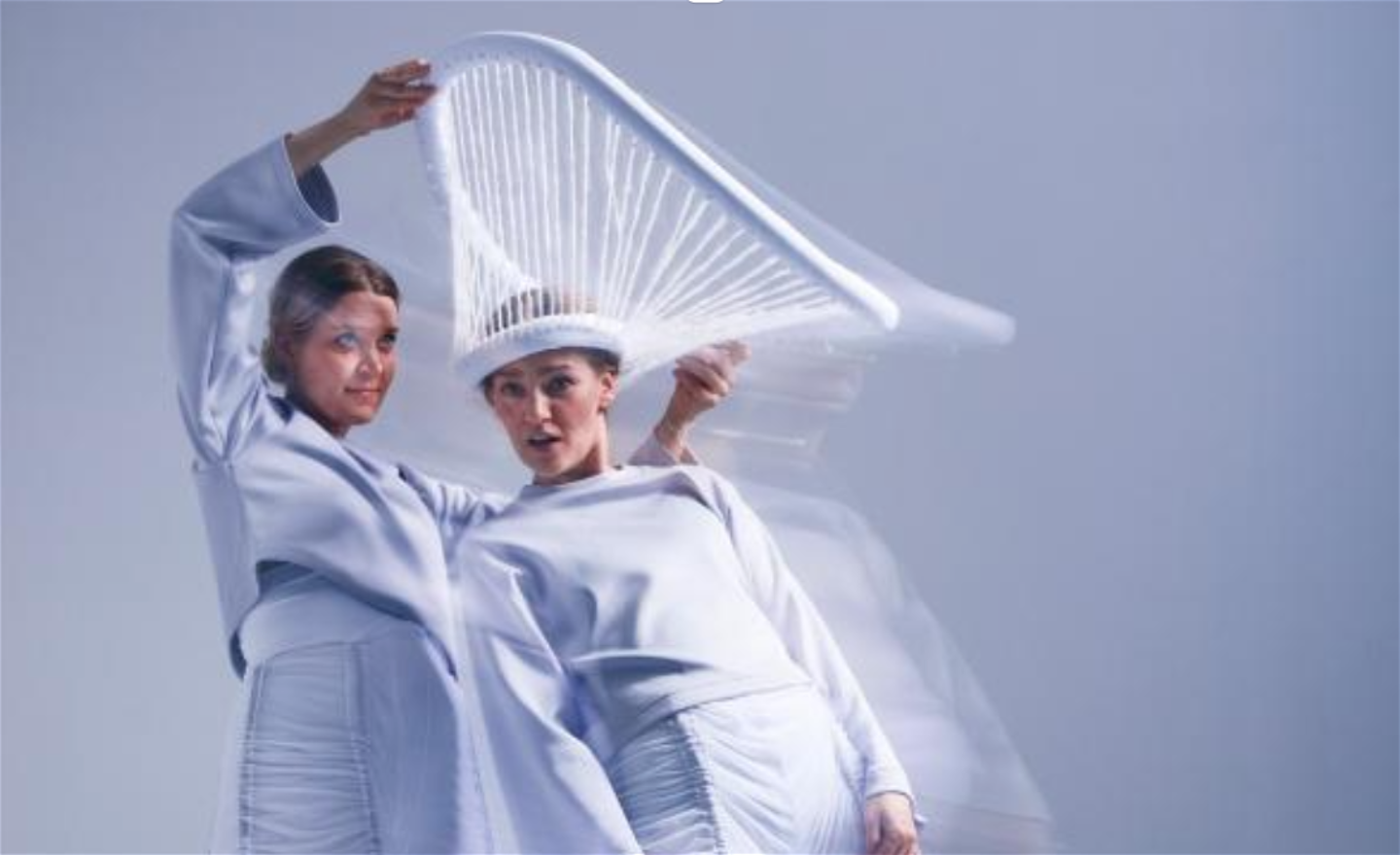Två vitklädda dansare. Den ena med överraska uppsyn och vit svamphatt på huvudet