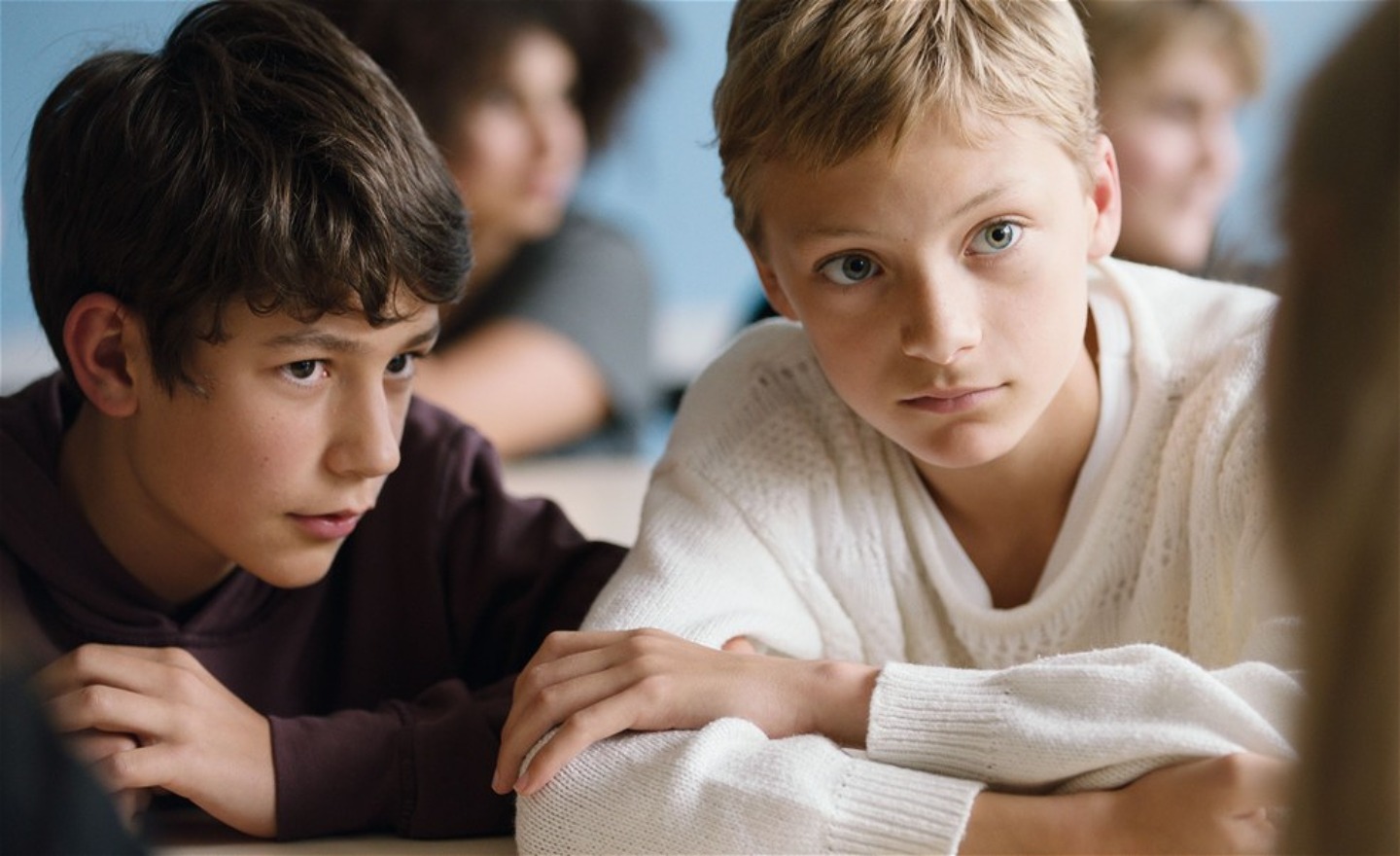 Två allvarliga pojkar sitter intill varandra med armarna på skolbänken och lyssnar koncentrerat.