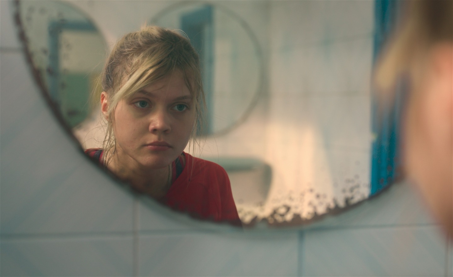 Allvarlig tonårsflicka speglar sig i en badrumsspegel.