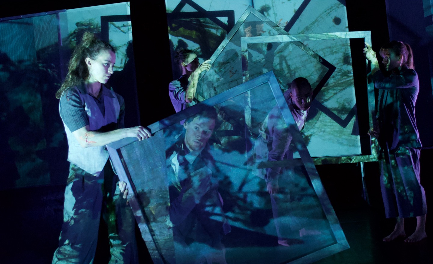 Fem dansare rör sig med eller mellan 1x1 m stora ramar i en blå-lila projektions- o ljusmiljö