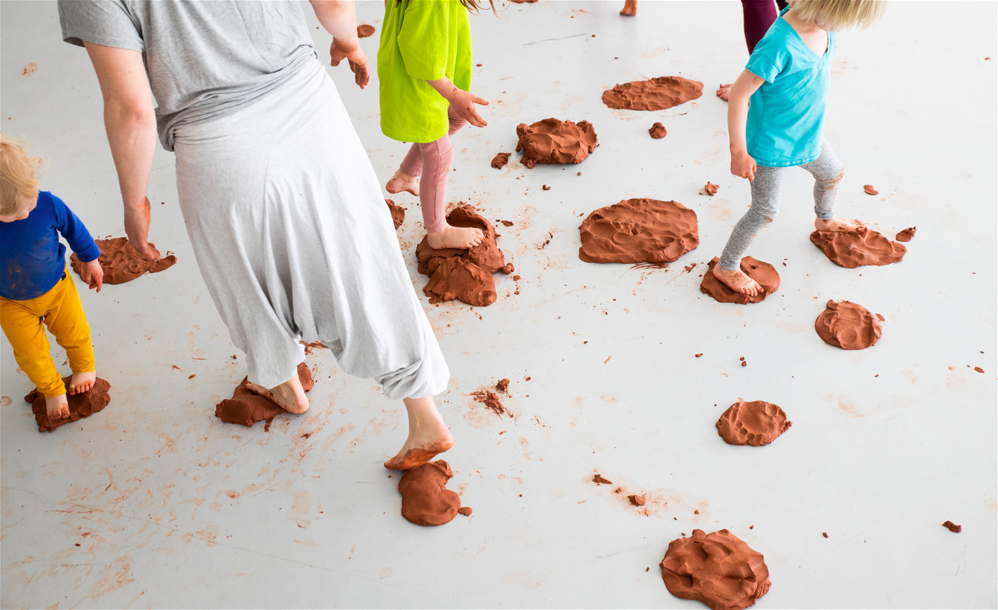 Barn och vuxna som rör sig över öar av lera på golvet.