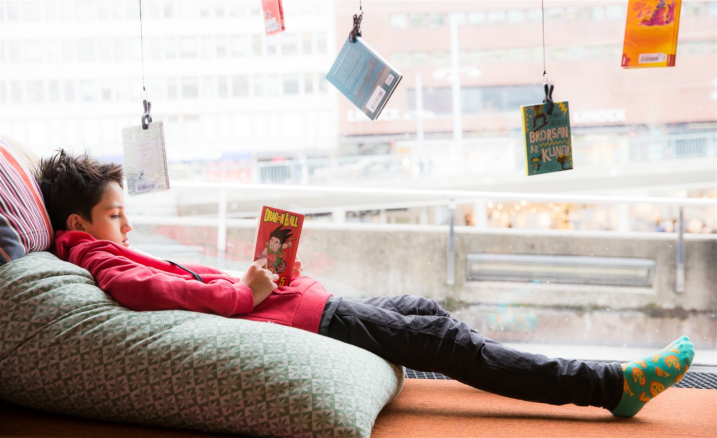 En kille ligger utsträckt på en kudde och läser en bok på bibliotek TioTretton