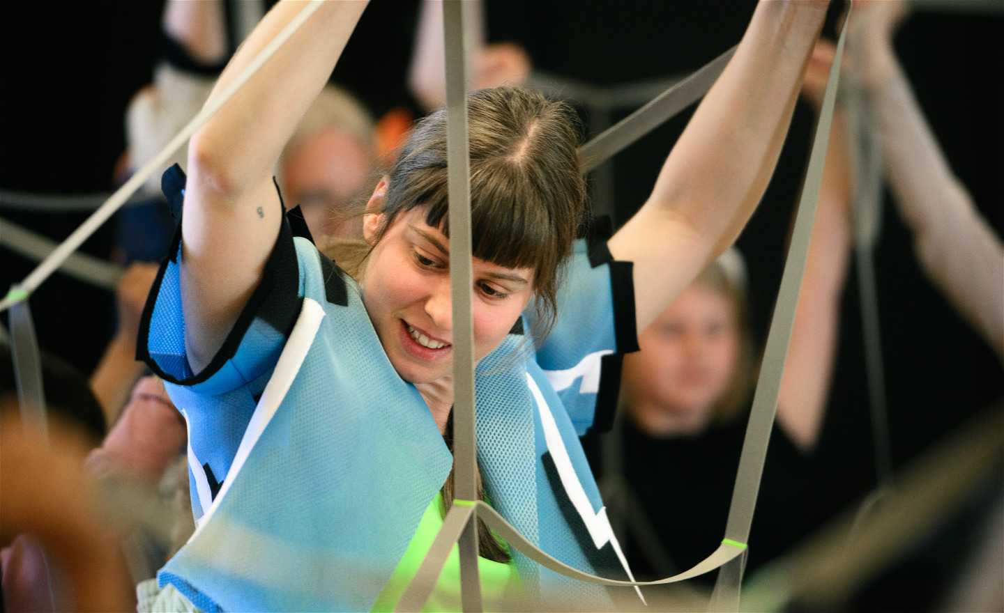 En dansare håller upp ett elastiskt nät. I bakgrunden och förgrunden skymtar barn som också håller upp nätet. 