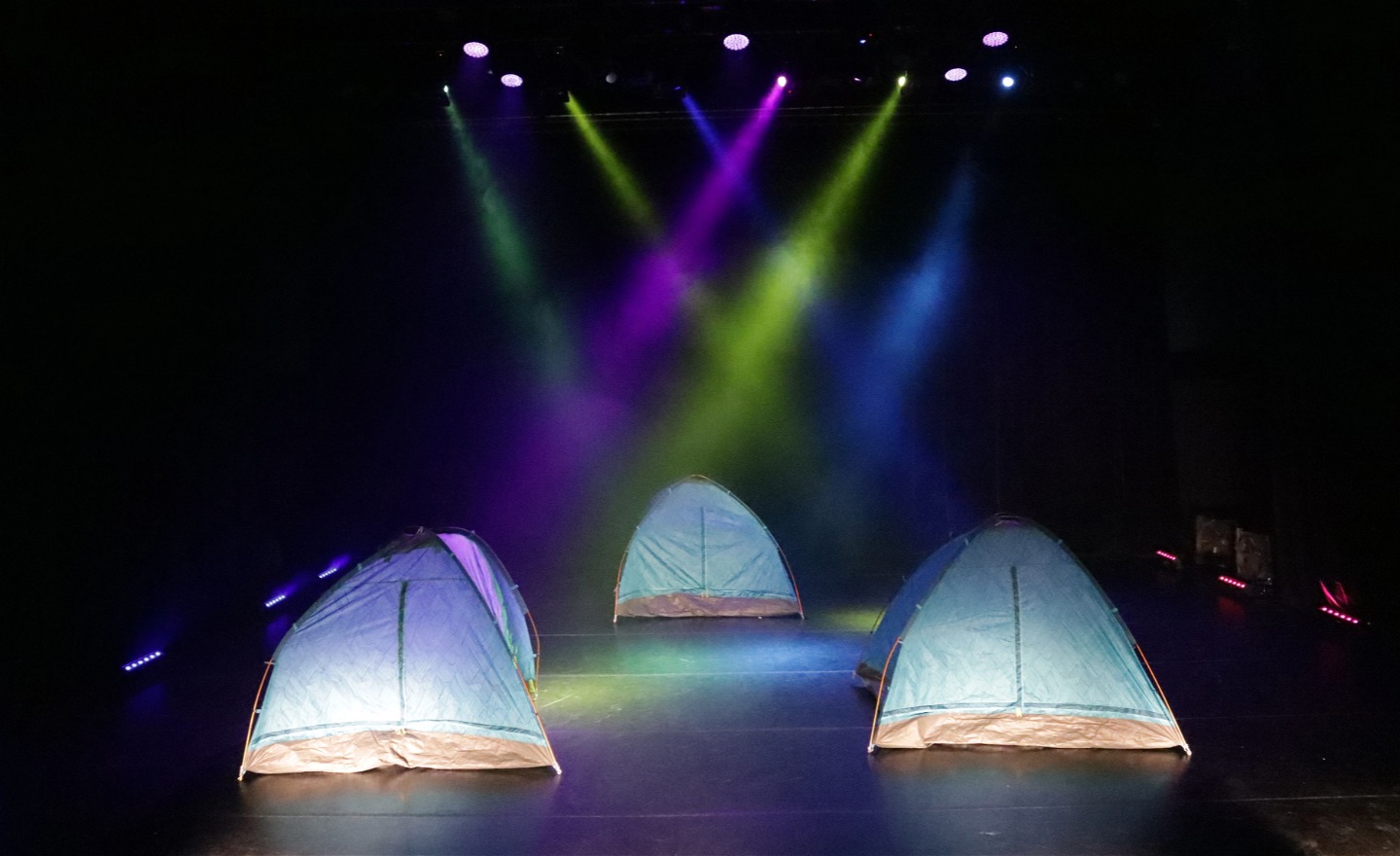 Tre silvriga tält på en scen med strålkastarljus i olika färger