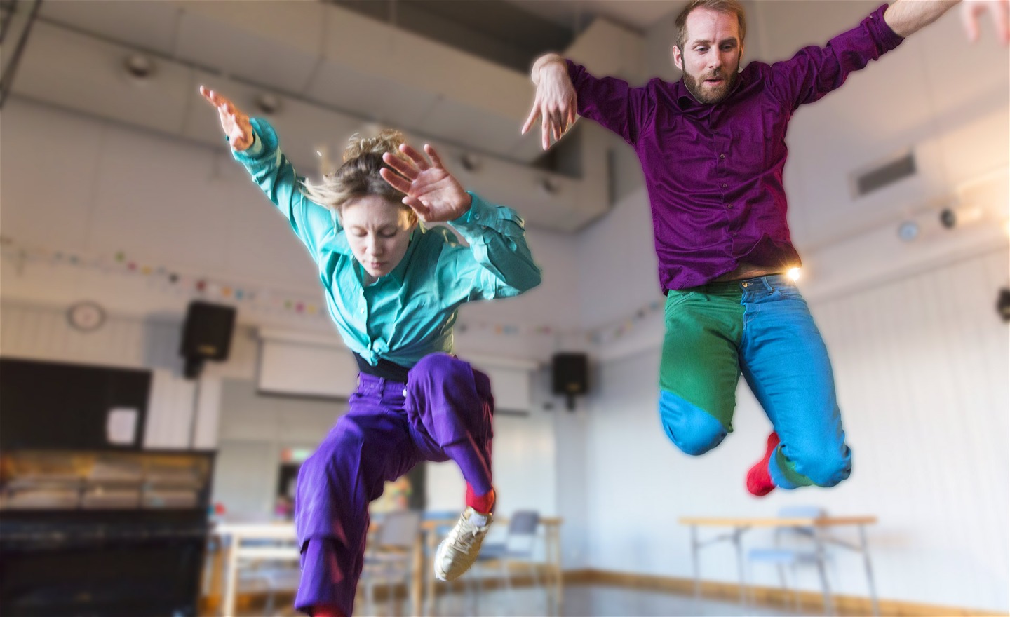 En kvinnlig och manlig dansare som dansar och hoppar över skolbänkarna i klassrummet