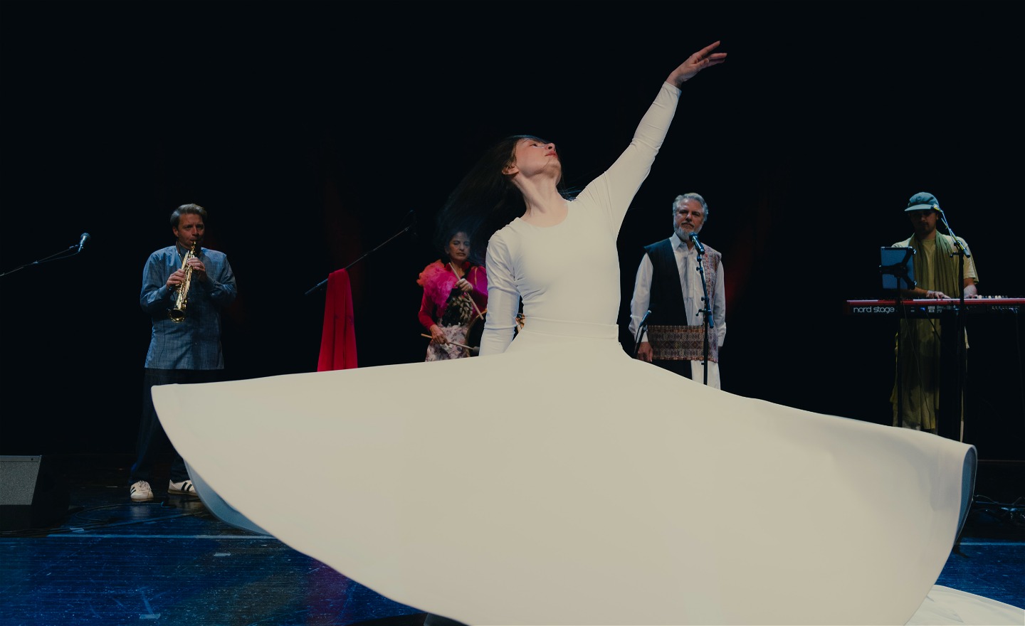 En bild där dansaren (i gruppen Golbang) står i mitten och dansar sufisk dans samtidigt som resterande bandmedlemmar står i bakgrunden och ackompanjerar.