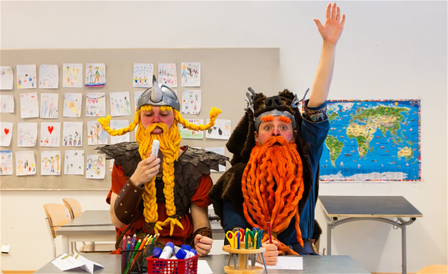 Två vikingar sitter i ett klassrum. Den ena slickar på ett limstift och den andra räcker upp handen