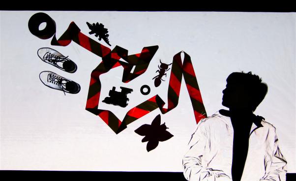 En dansare och olika föremål som ett par skor, en fjäril och ett avspärrningsband skapar siluetter mot ett reflextyg.