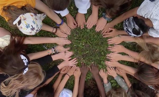 Barnhänder tätt intill varandra på marken i en cirkel. Bild tagen ovanifrån.