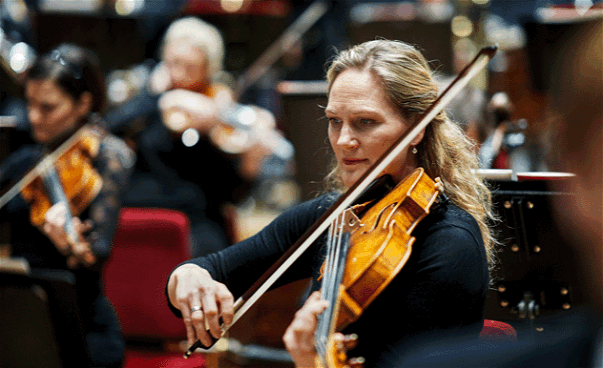 Kvinna som spelar på en fiol under konsert. Fotografi.